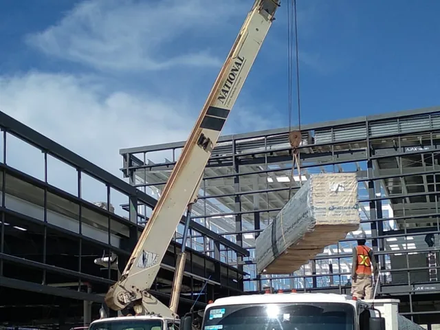 Maniobra con grúa montando un paquete de panel sobre la estructura metálica de la obra